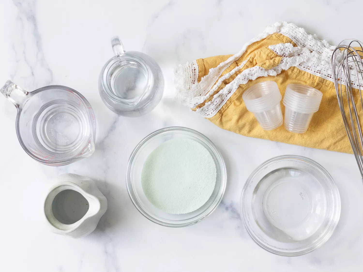 Ingredients for margarita jello shots including gelatin, water, and small serving cups arranged on a table