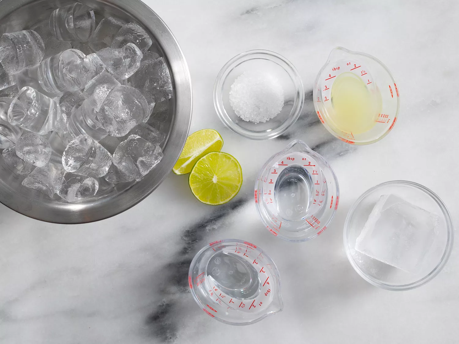 Overhead of a bowl of ice and margarita ingredients in various measuring cups.