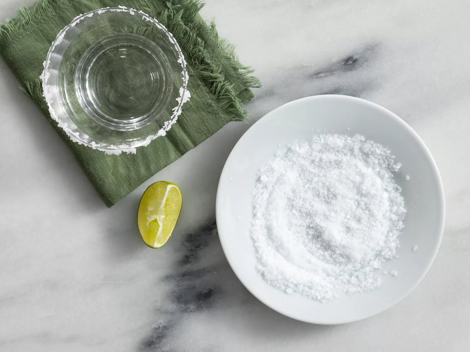 Overhead of a salted rimmed glass, a plate of salt, and lime wedge. 