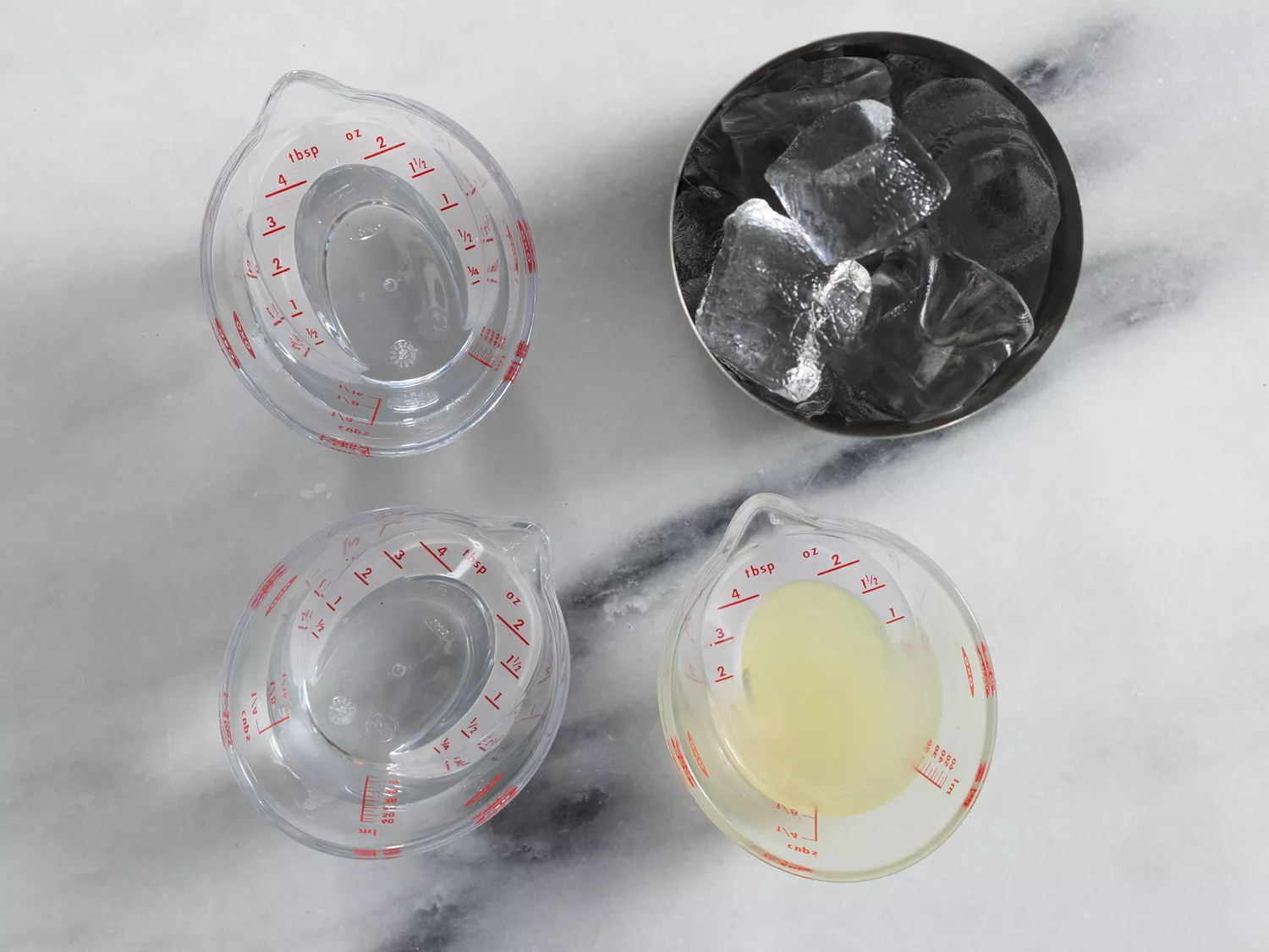 Overhead of a shaker full of ice and three measuring cups filled with different margarita ingredients. 