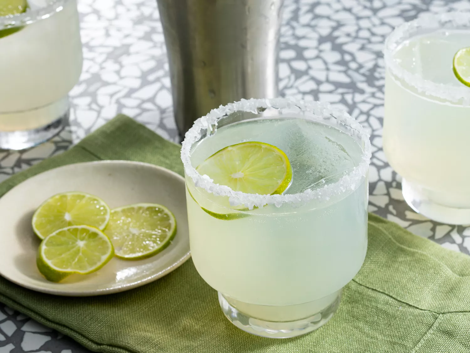 Mid angle looking at a glass of margarita garnished with lime slices