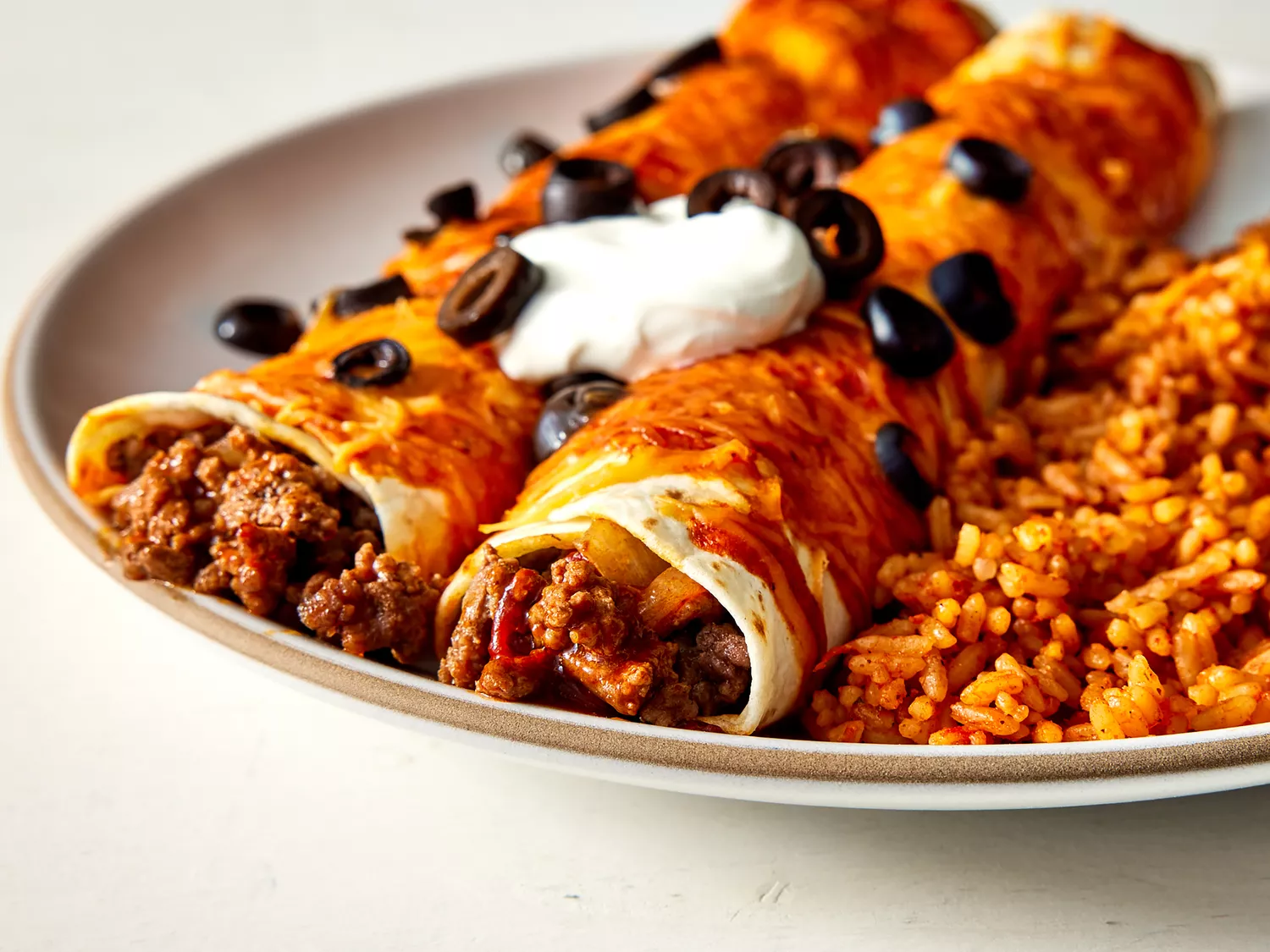 A low angle view looking at two plated beef enchiladas with a side of spanish rice.