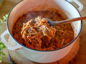 Pulled pork in a slow cooker with some on a wooden spoon