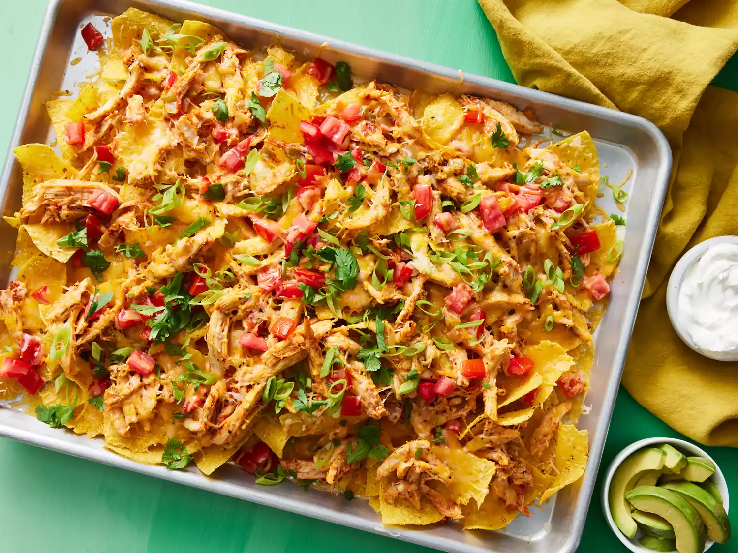 An overhead view of cheesy restaurant style nachos topped with diced tomatoes, sliced green onions, and cilantro.
