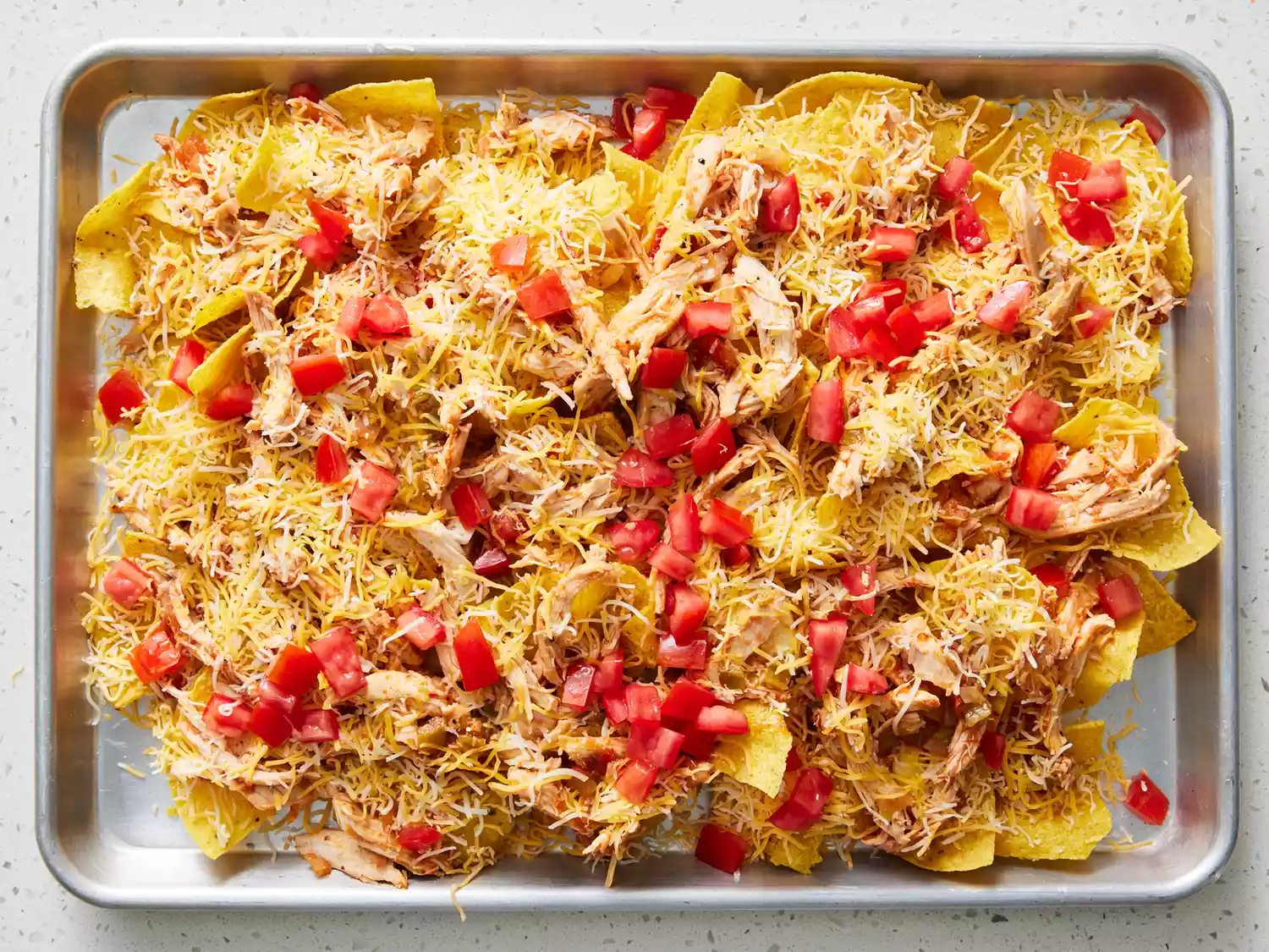 an overhead view of restaurant style nachos on a baking sheet prior to being baked 