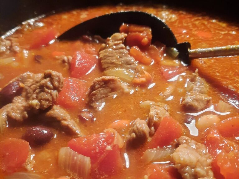 Close up view of chuck roast chili with tomatoes in a pot with a spoon