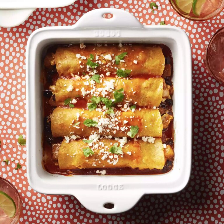 A white square casserole dish of roasted butternut squash and black bean enchiladas