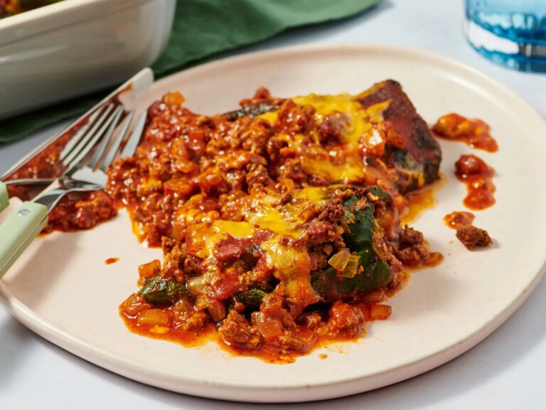 Stuffed poblano pepper topped with melted cheese and served with a tomato and beefbased sauce on a plate