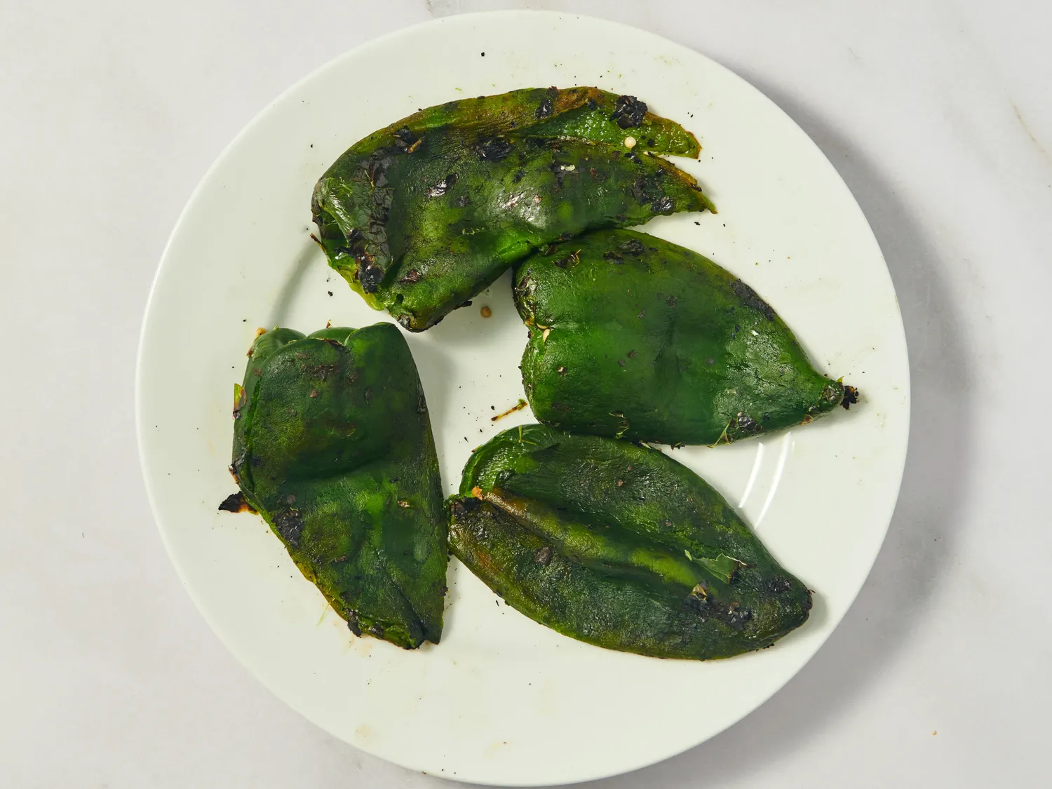 Four roasted poblano peppers placed on a white plate