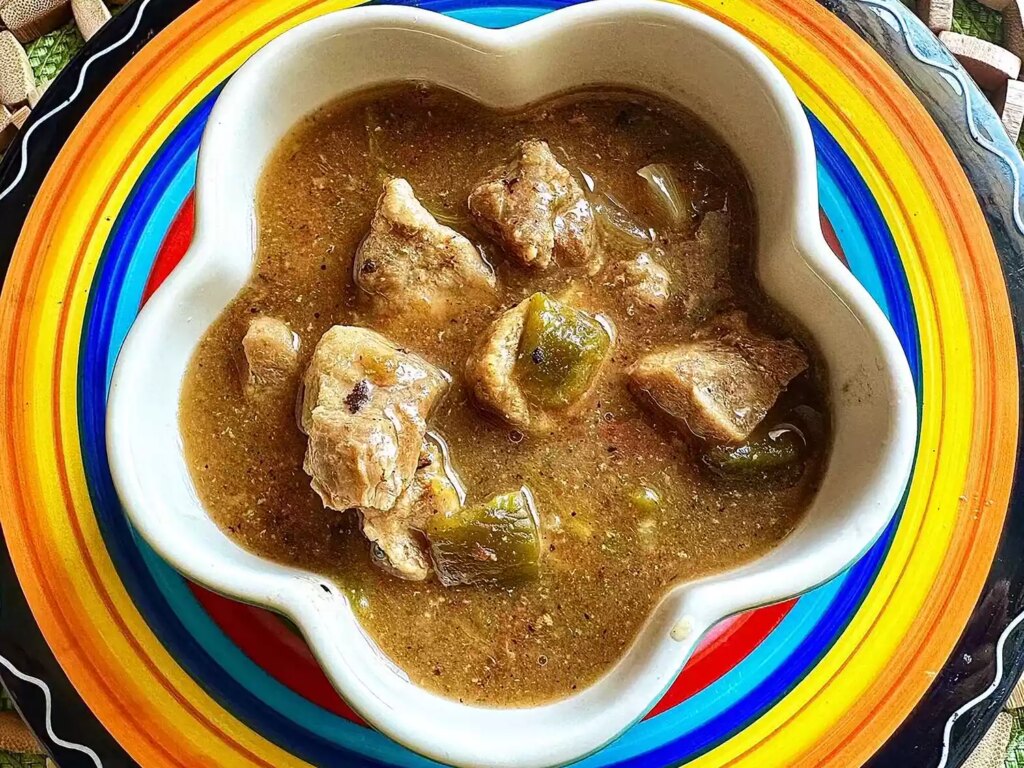 Pork chili verde in flower shaped white bowl set on colorful plate