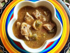 Pork chili verde in flower shaped white bowl set on colorful plate