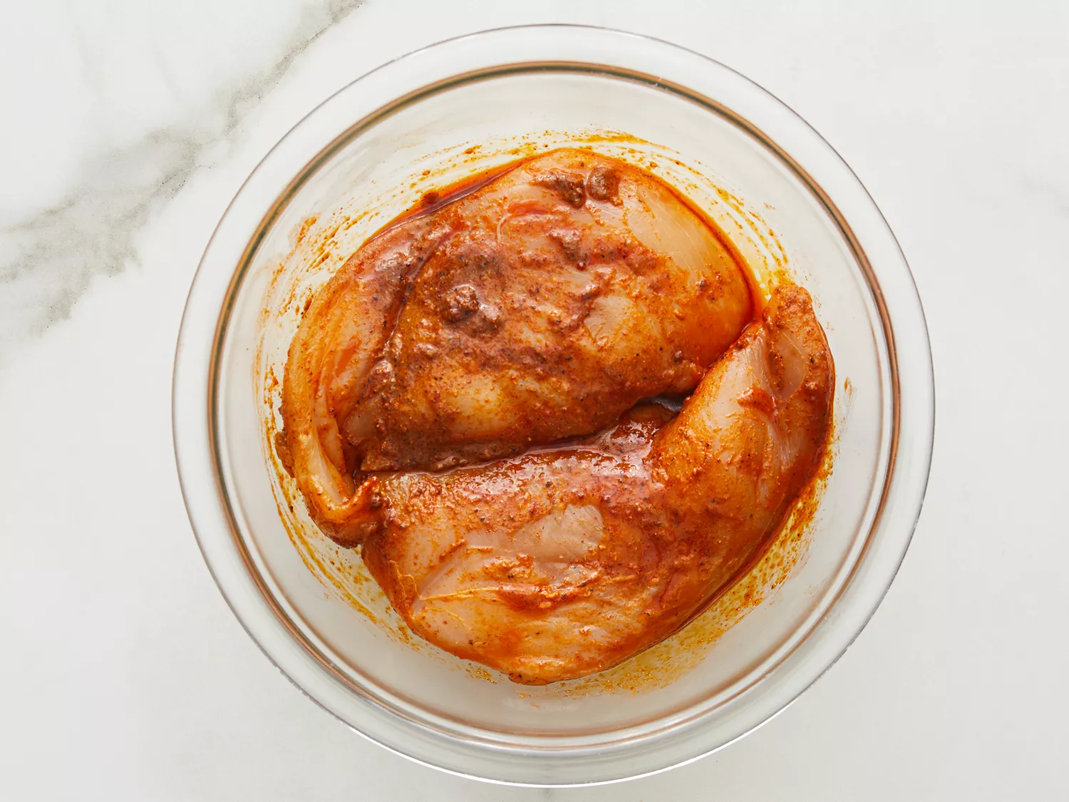 an overhead view of seasoned chicken breasts in a glass mixing bowl. 