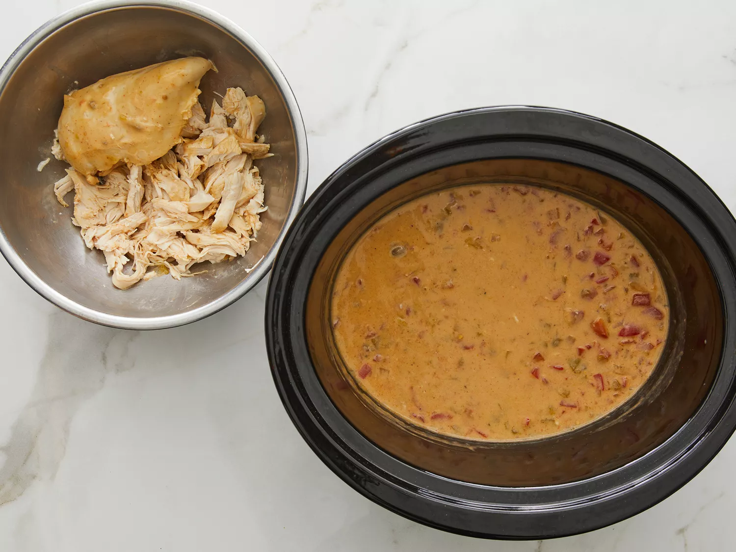 chicken, after being cooked, being shredded and ready to add back into a slow cooker. 