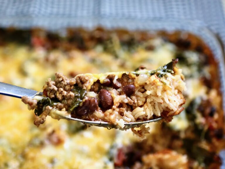 Close up of spoon with beef, rice, and beans casserole topped with cheese