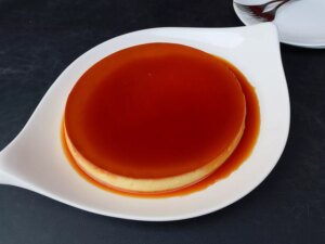 Instant pot bahn flan (vietnamese flan) on a white serving platter with a deeply colored caramel sauce pooling around the custard