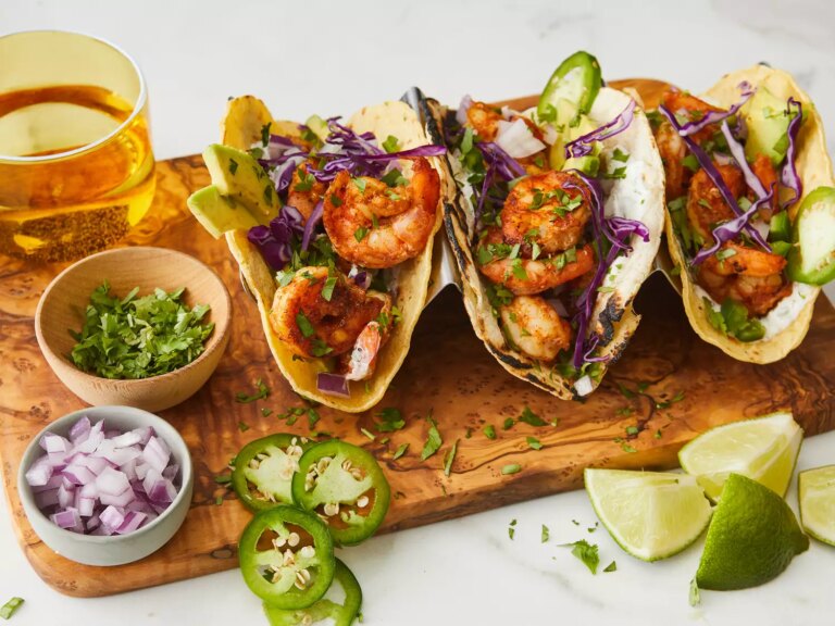 A close up on three shrimp tacos with cilantro lime crema on a taco stand.