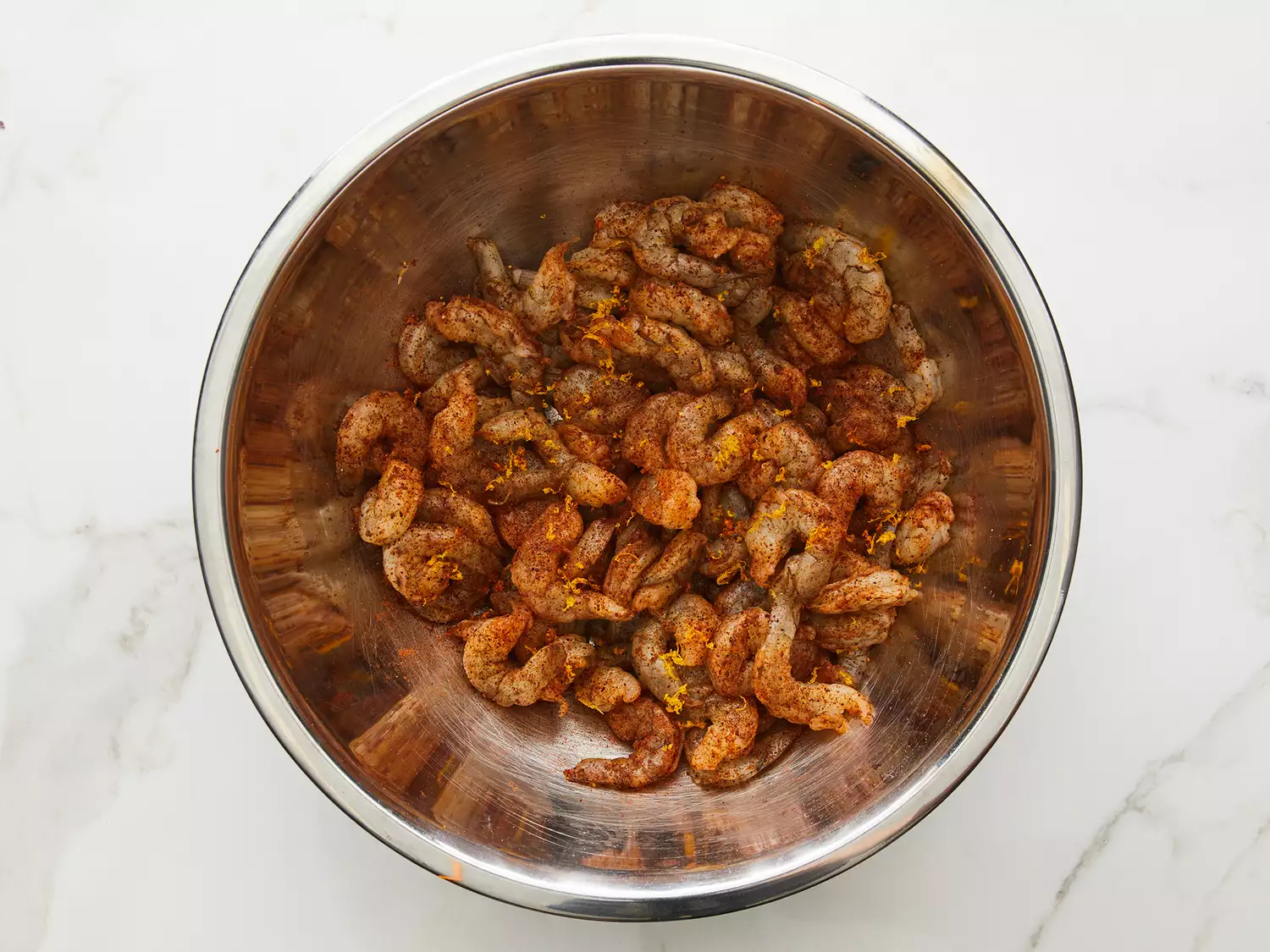 Overhead of shrimp being mixed with a chili powder mixture in a bowl. 