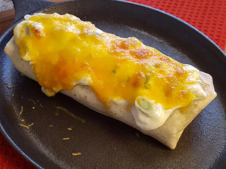 Close up view of a smothered burrito topped with cheese on a black plate