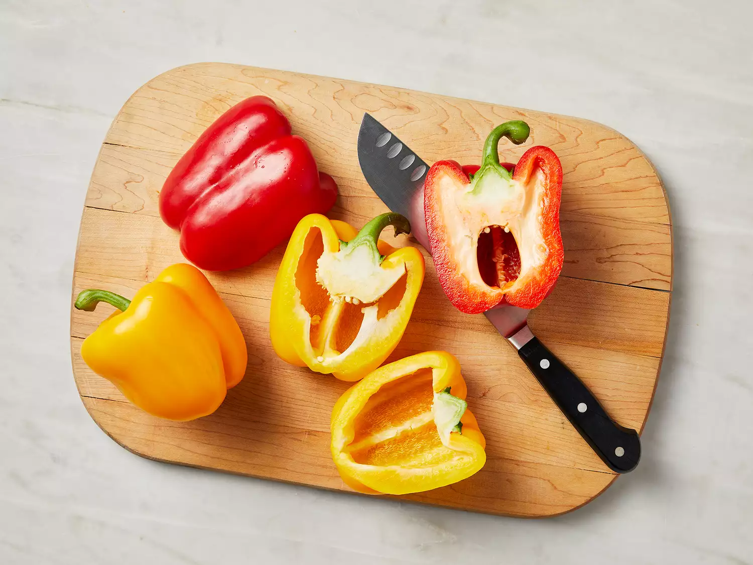 Overhead of a red and a yellow bell pepper being cut in half on a cutting board. 