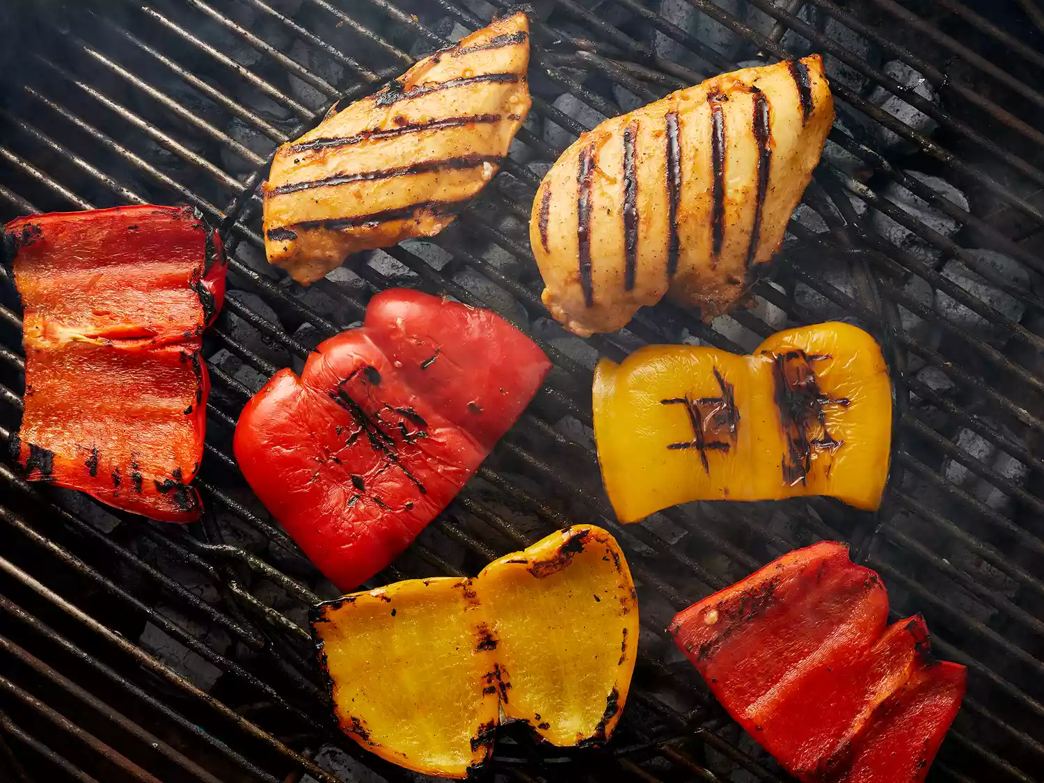 Overhead of chicken and bell peppers cooking on a grill. 