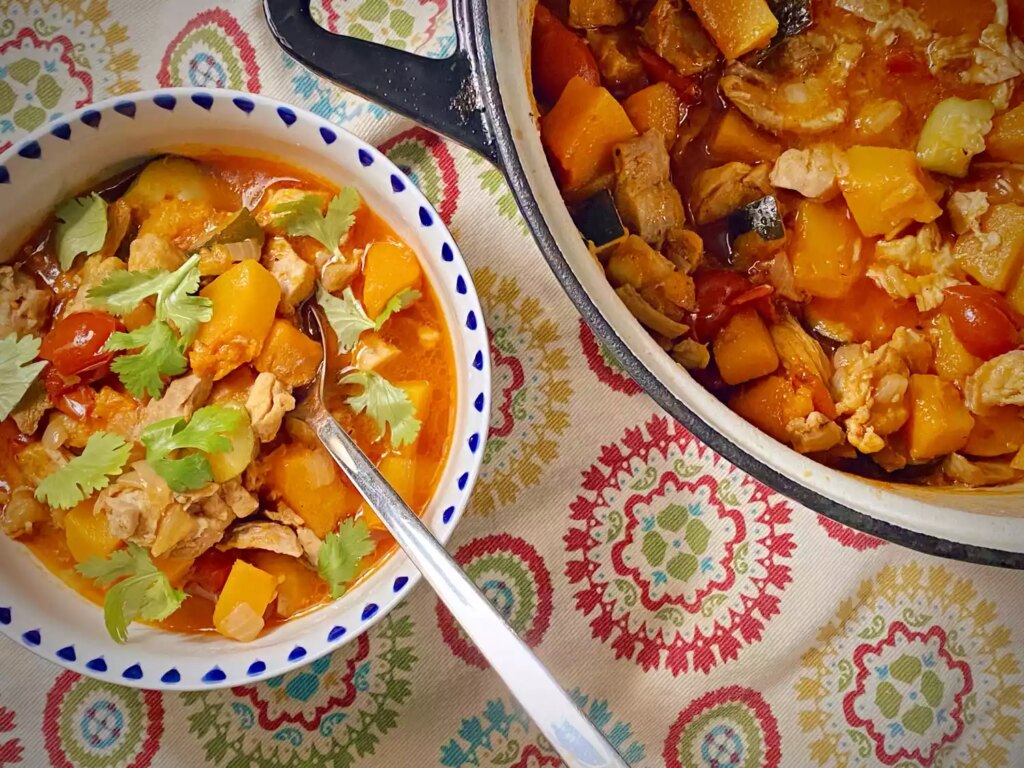Calabaza squash and chicken in bowl garnished with cilantro and large pot on the side