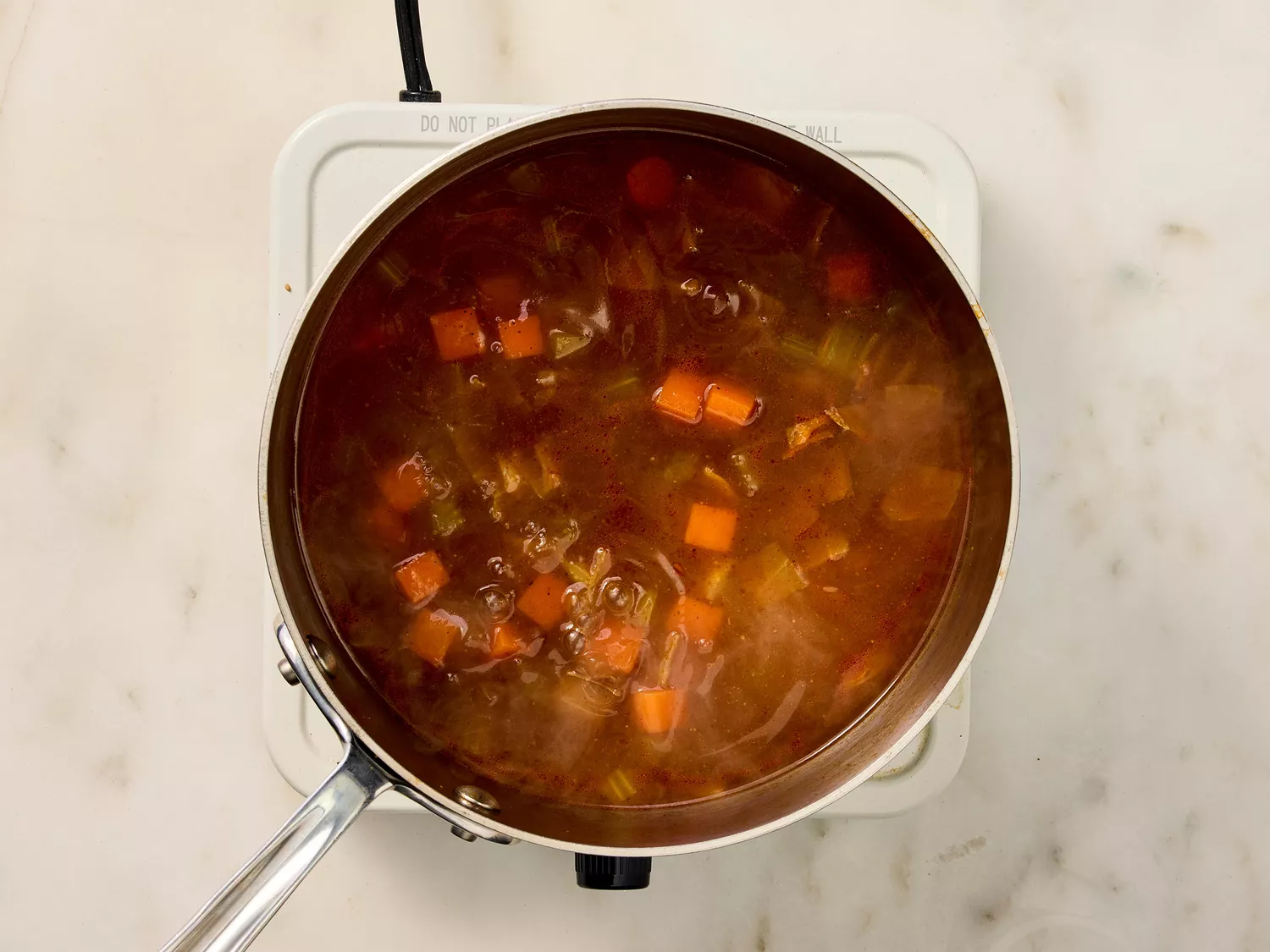 Simmering pot of birria consommé with vegetables.