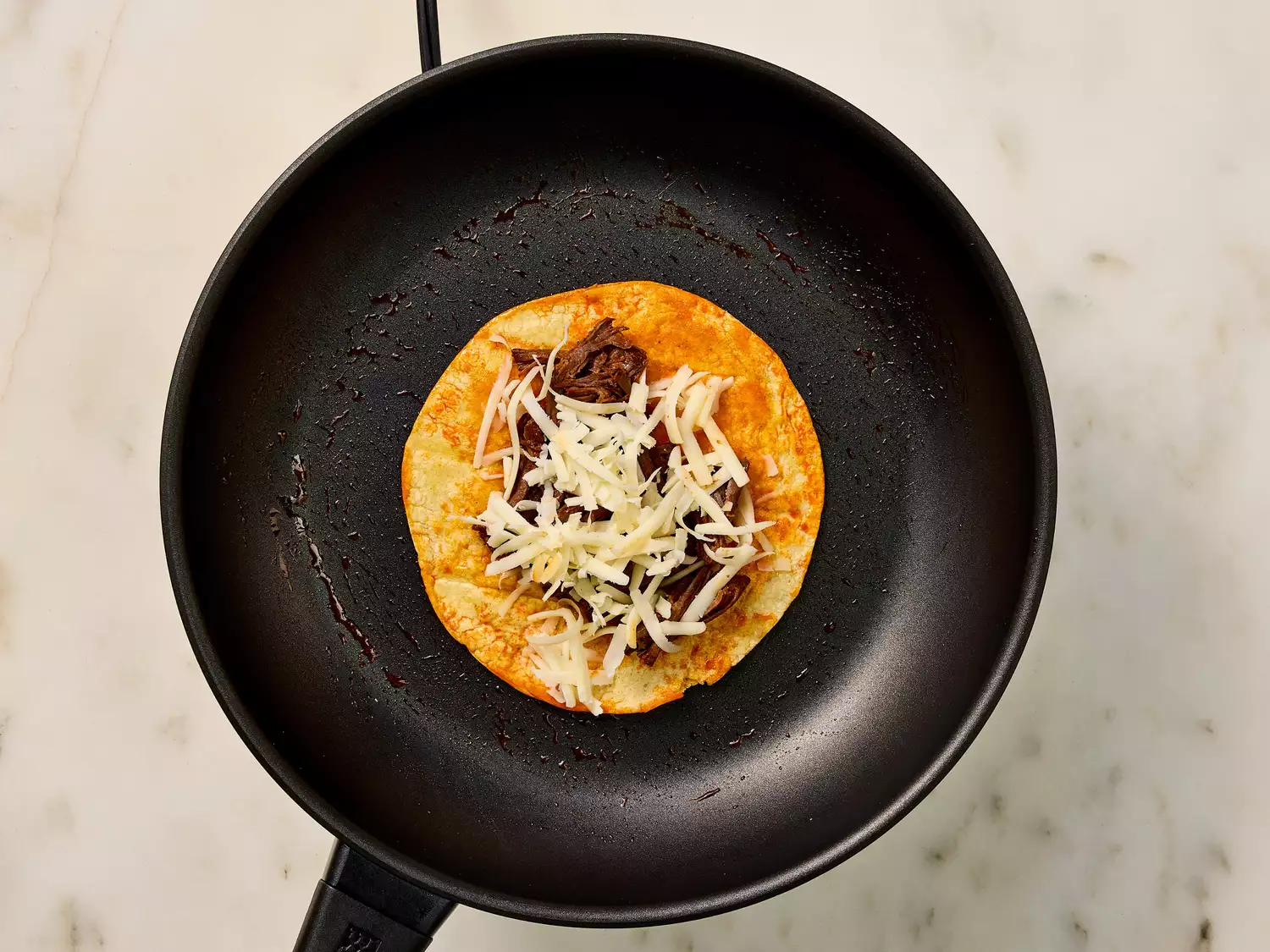 Corn tortilla with beef and cheese in a frying pan.