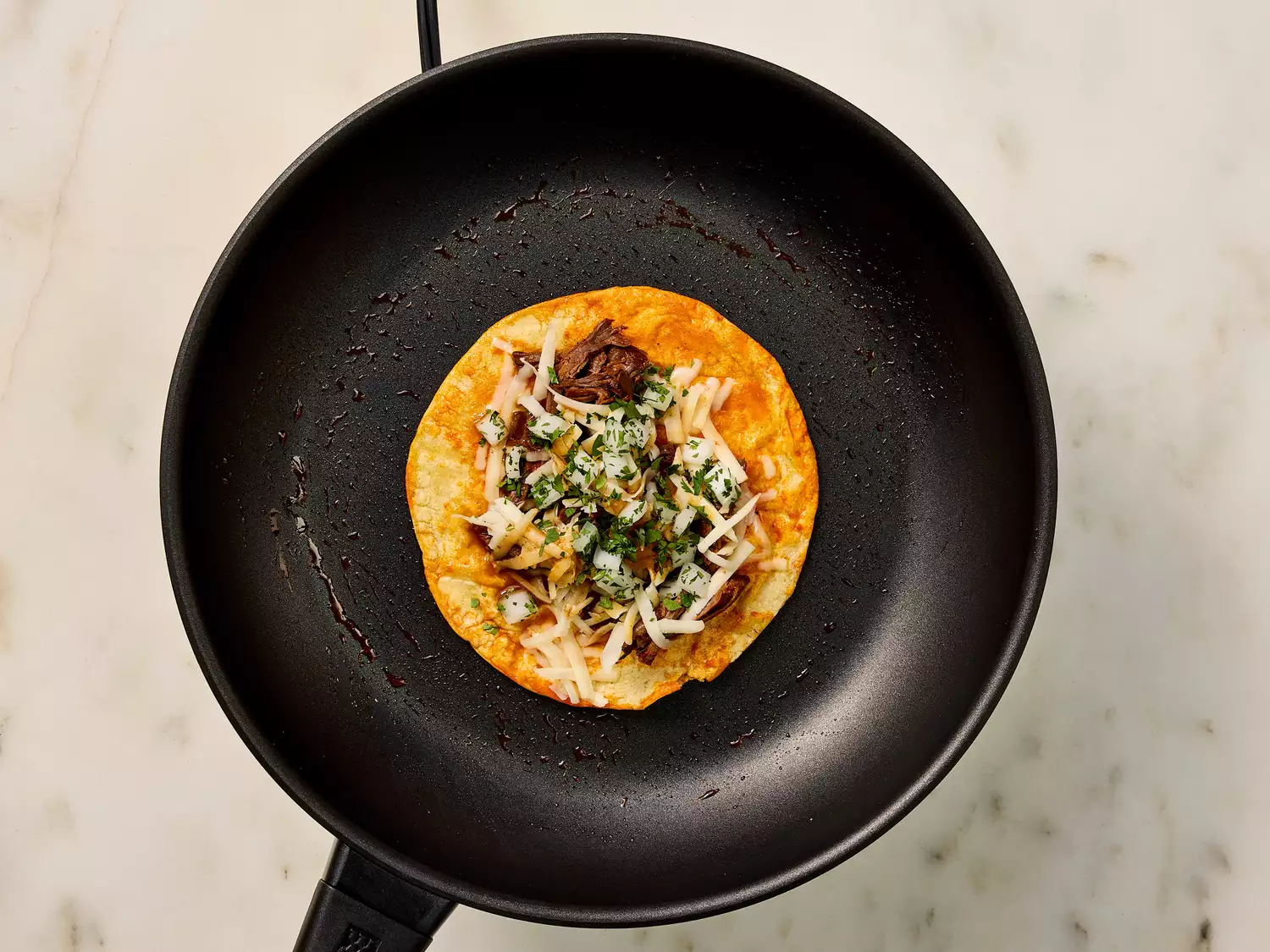 Birria taco in a pan with chopped onions and cilantro.