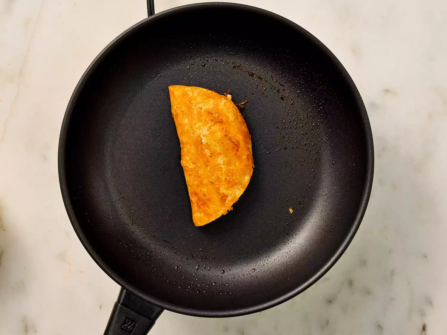 Folded birria taco frying in a pan.