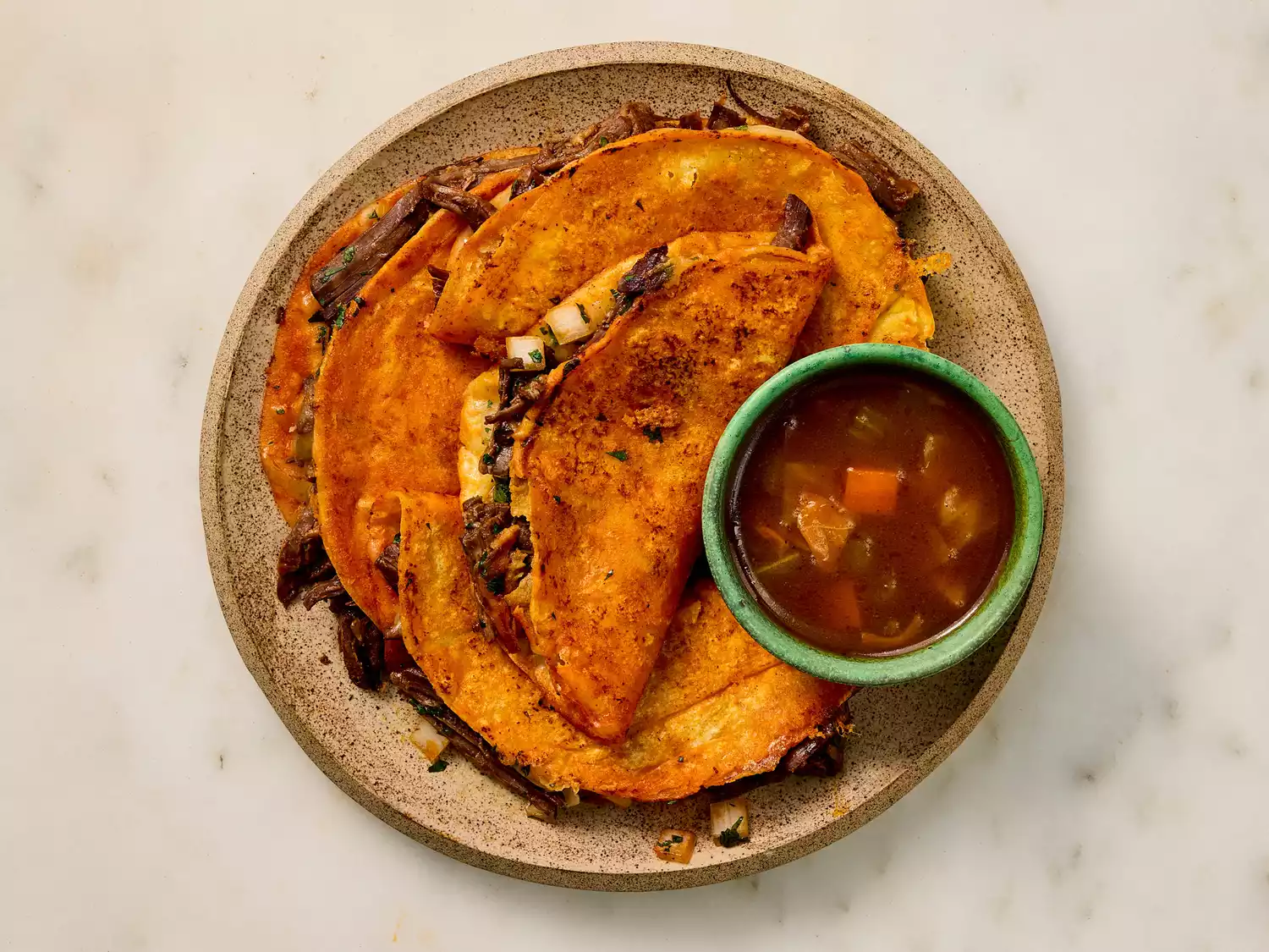 Plate of birria tacos served with a bowl of consommé.