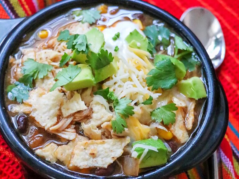 Chicken tortilla soup garnished with avocado, cheese, and cilantro