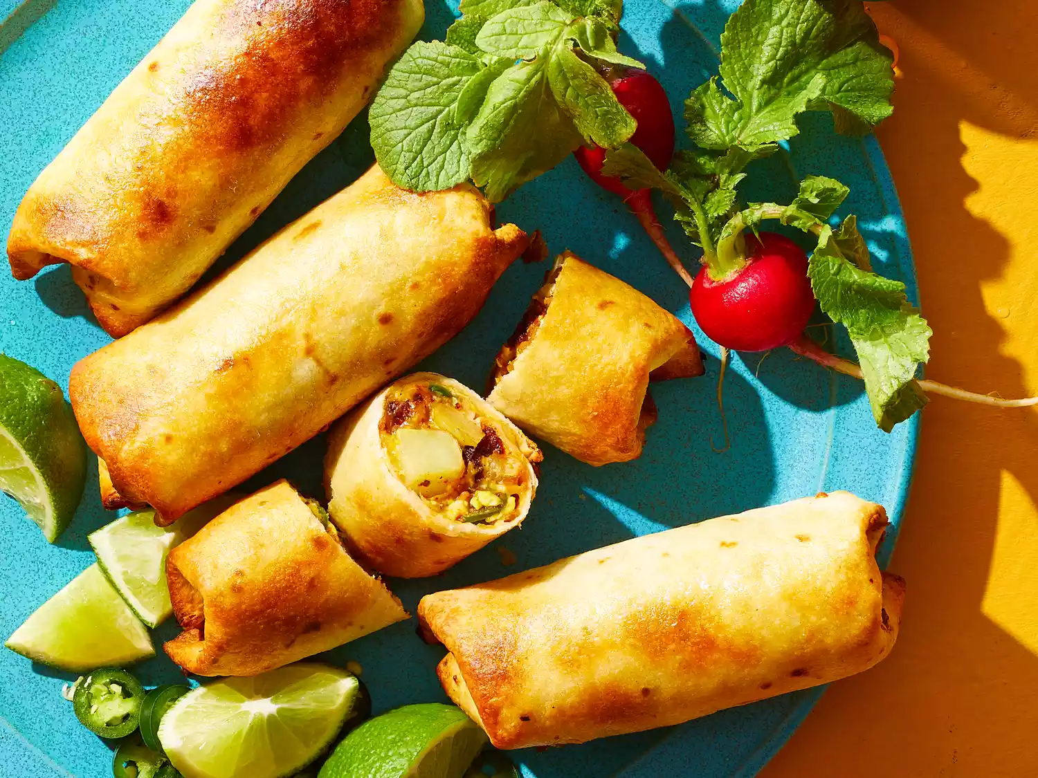 An overhead shot of air fryer mini spicy breakfast burritos with limes and radishes