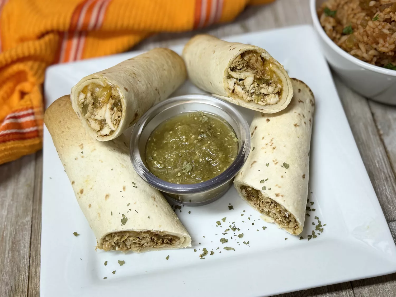 Baked chicken and cheese flautas on white plate with green salsa for dipping