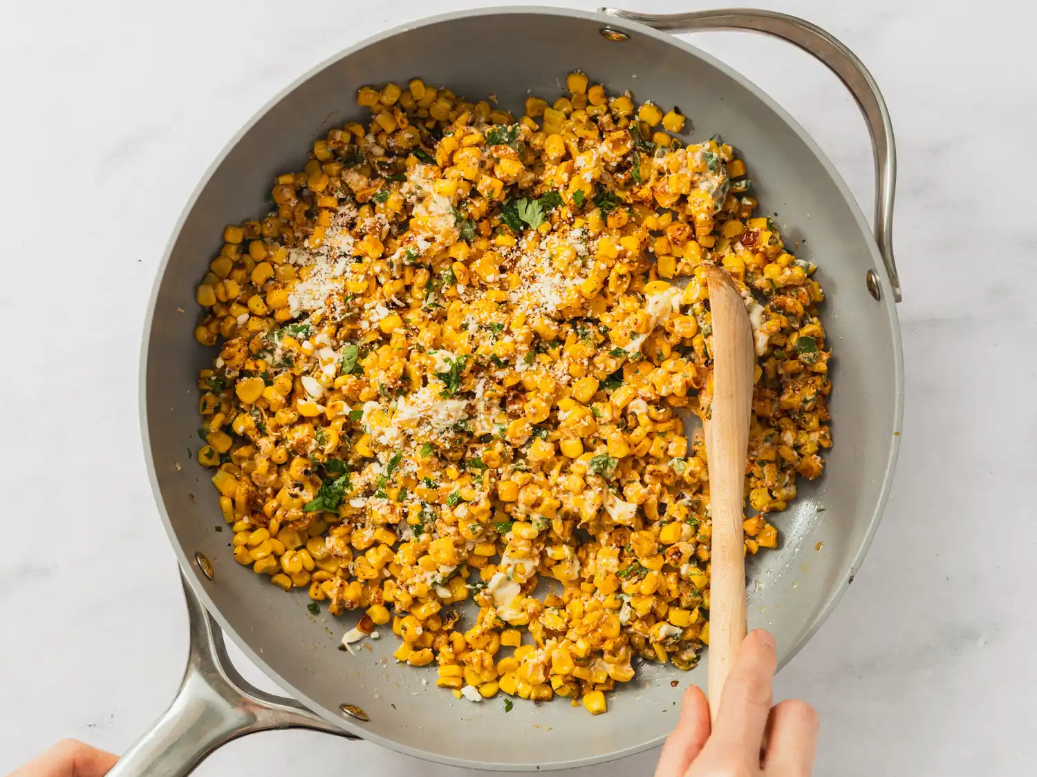 A pan containing Mexican street corn dip being stirred with a wooden spoon