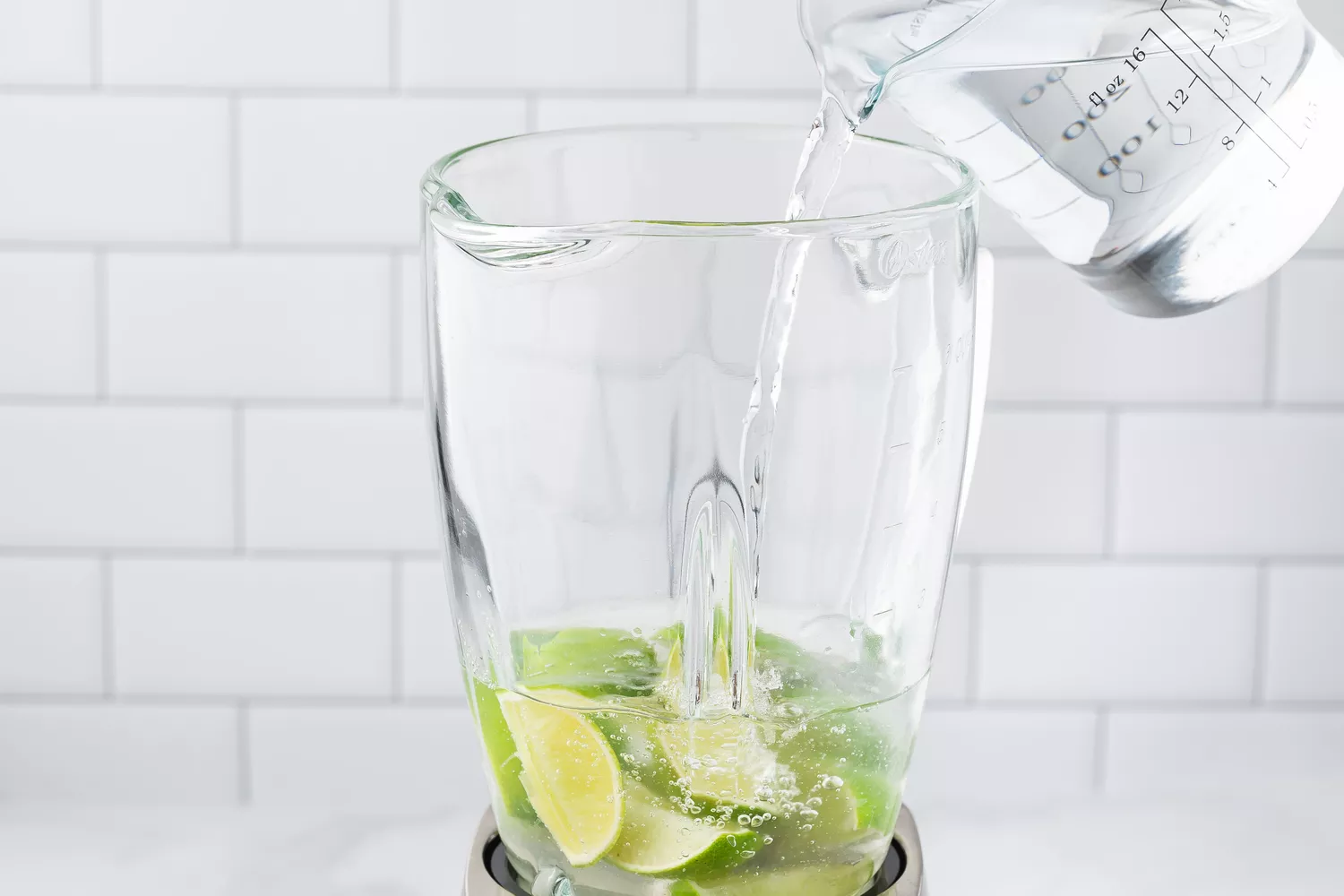 A person pouring water in a blender with lime wedges. 