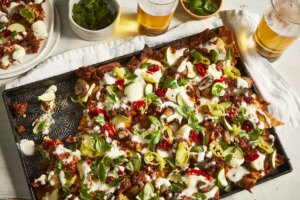 A tray of beefy lasagna nachos with a portion plated and served with a couple of beers