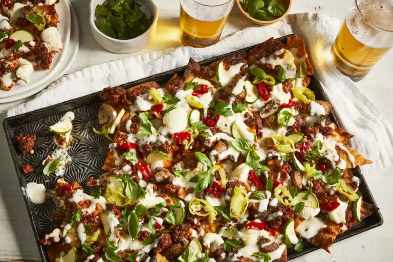A tray of beefy lasagna nachos with a portion plated and served with a couple of beers