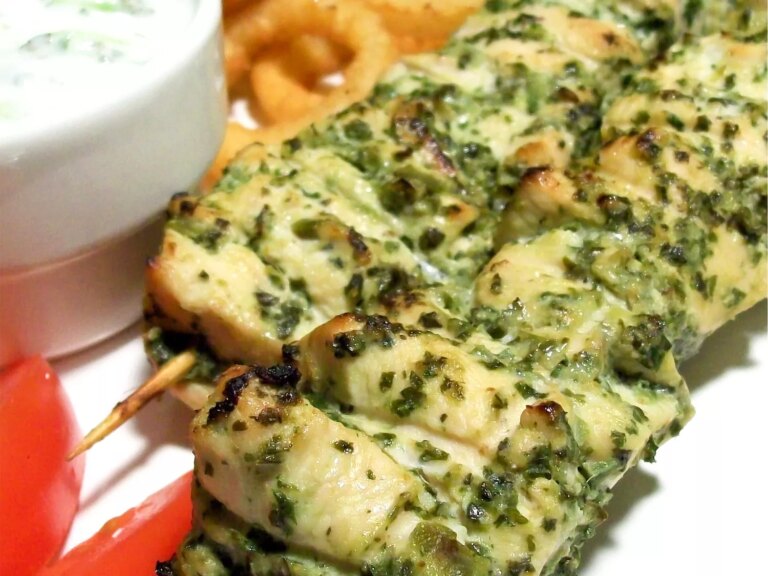 Close up view of chicken hariyali tikka skewers next to sauce in a sauce cup