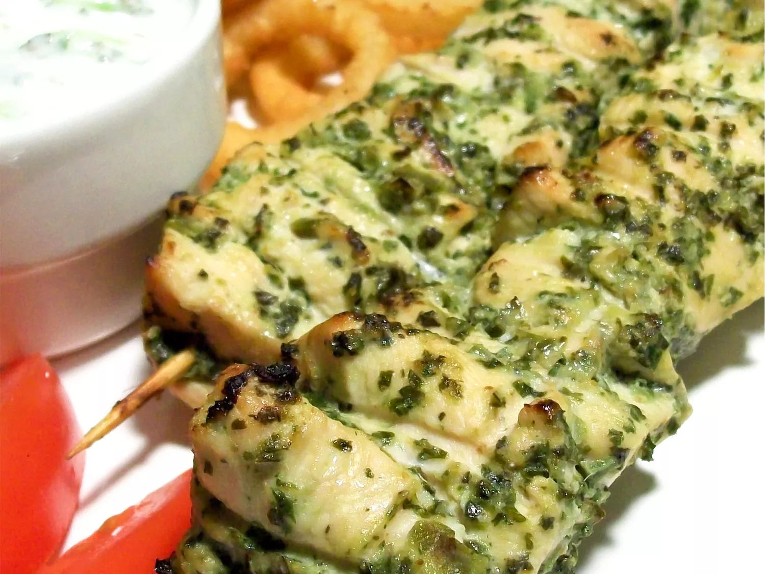 Close up view of chicken hariyali tikka skewers next to sauce in a sauce cup
