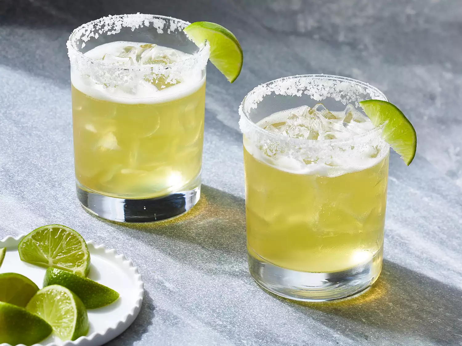 Close up on two glasses of margaritas on the rocks, garnished with a lime wedge