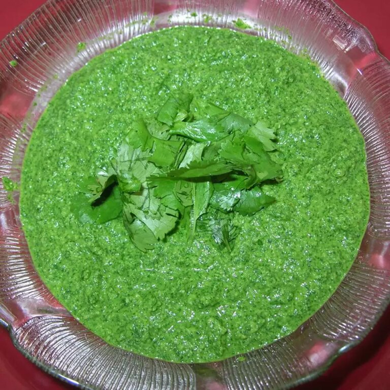 Close up view of green chutney in a glass bowl, garnished with fresh herbs