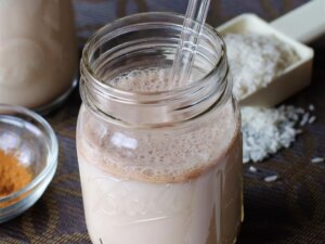 Close up view of horchata in a glass jar with a glass straw, next to cinnamon in bowl
