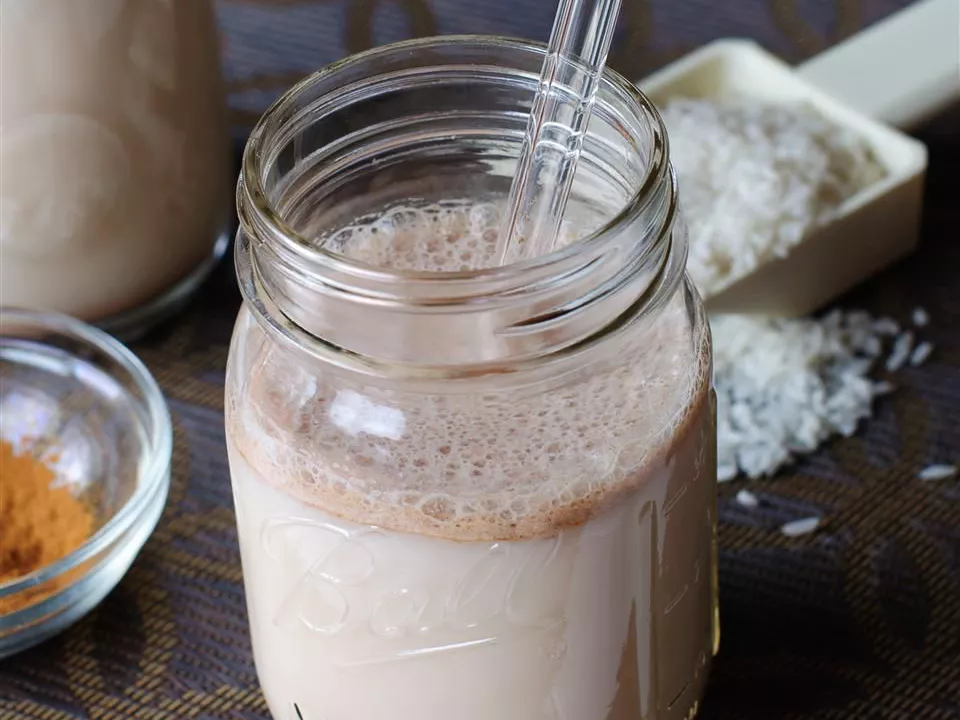 Close up view of horchata in a glass jar with a glass straw, next to cinnamon in bowl