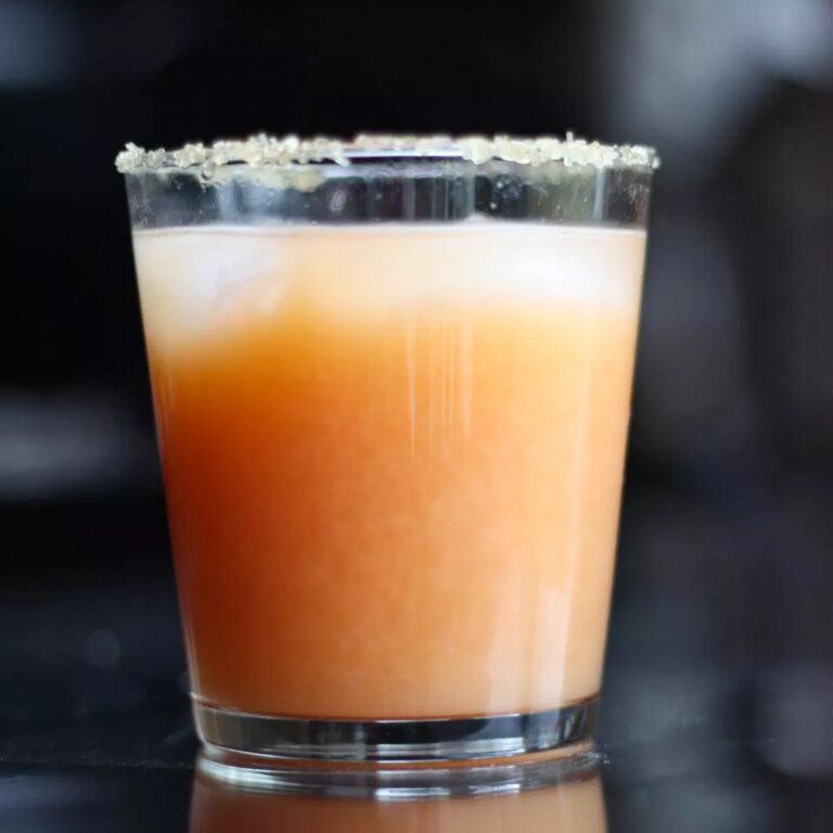 Close up view of a grapefruit margarita in a glass, garnished with salt on the rim
