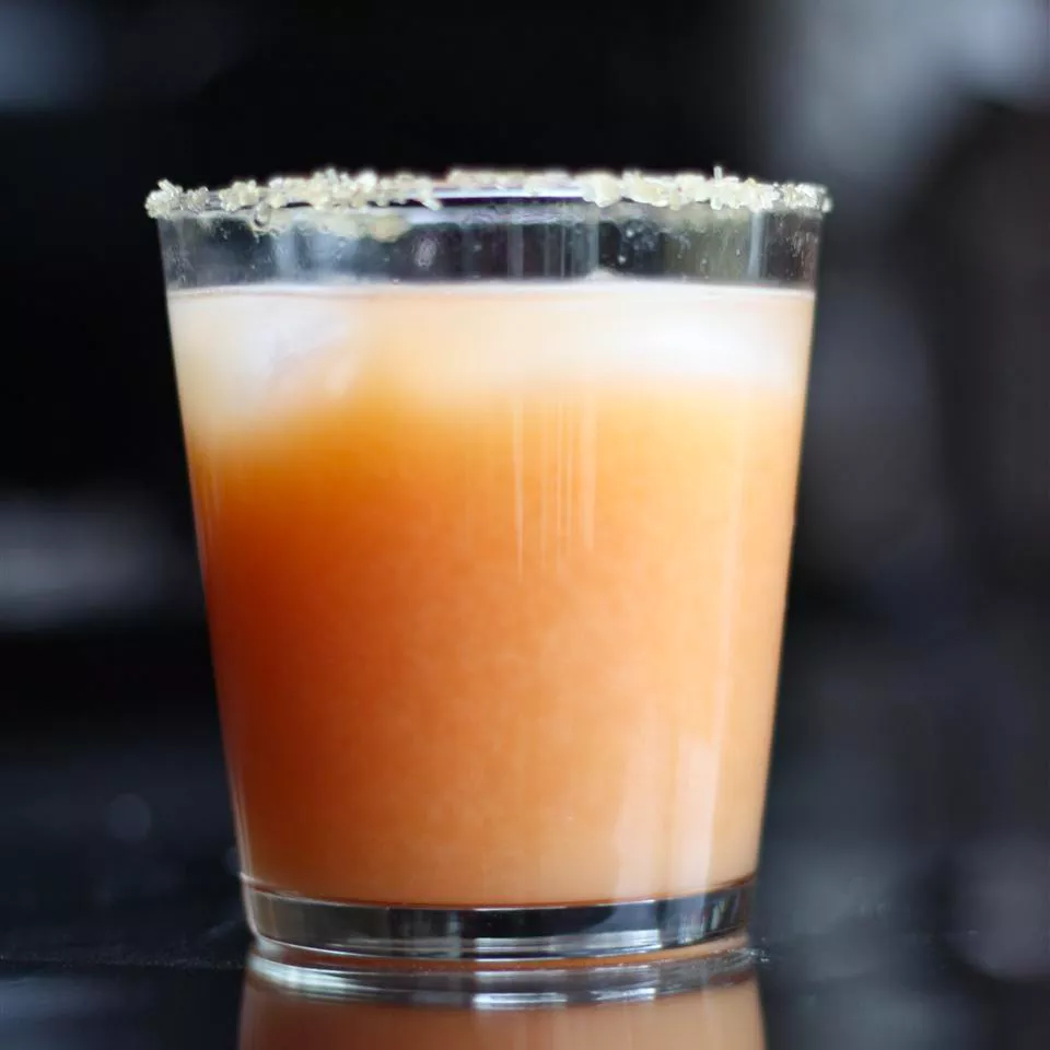Close up view of a grapefruit margarita in a glass, garnished with salt on the rim