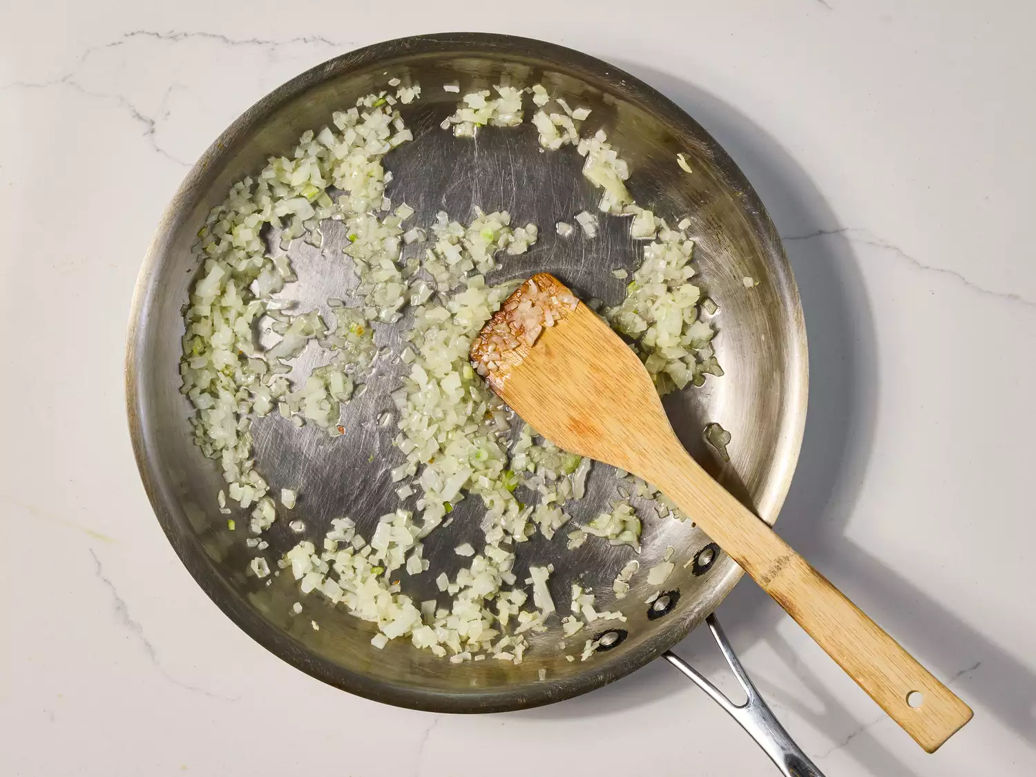 Chopped onions sautéing in a stainless steel pan.