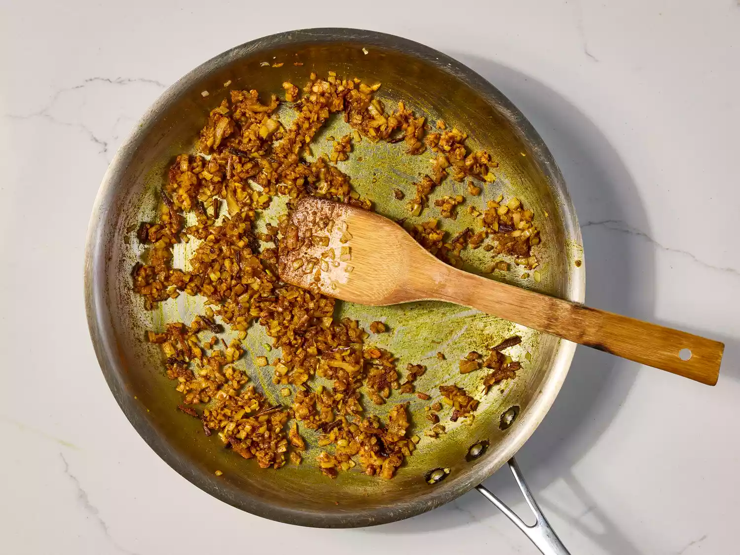 Spices and onions cooking in a pan with a wooden spatula.