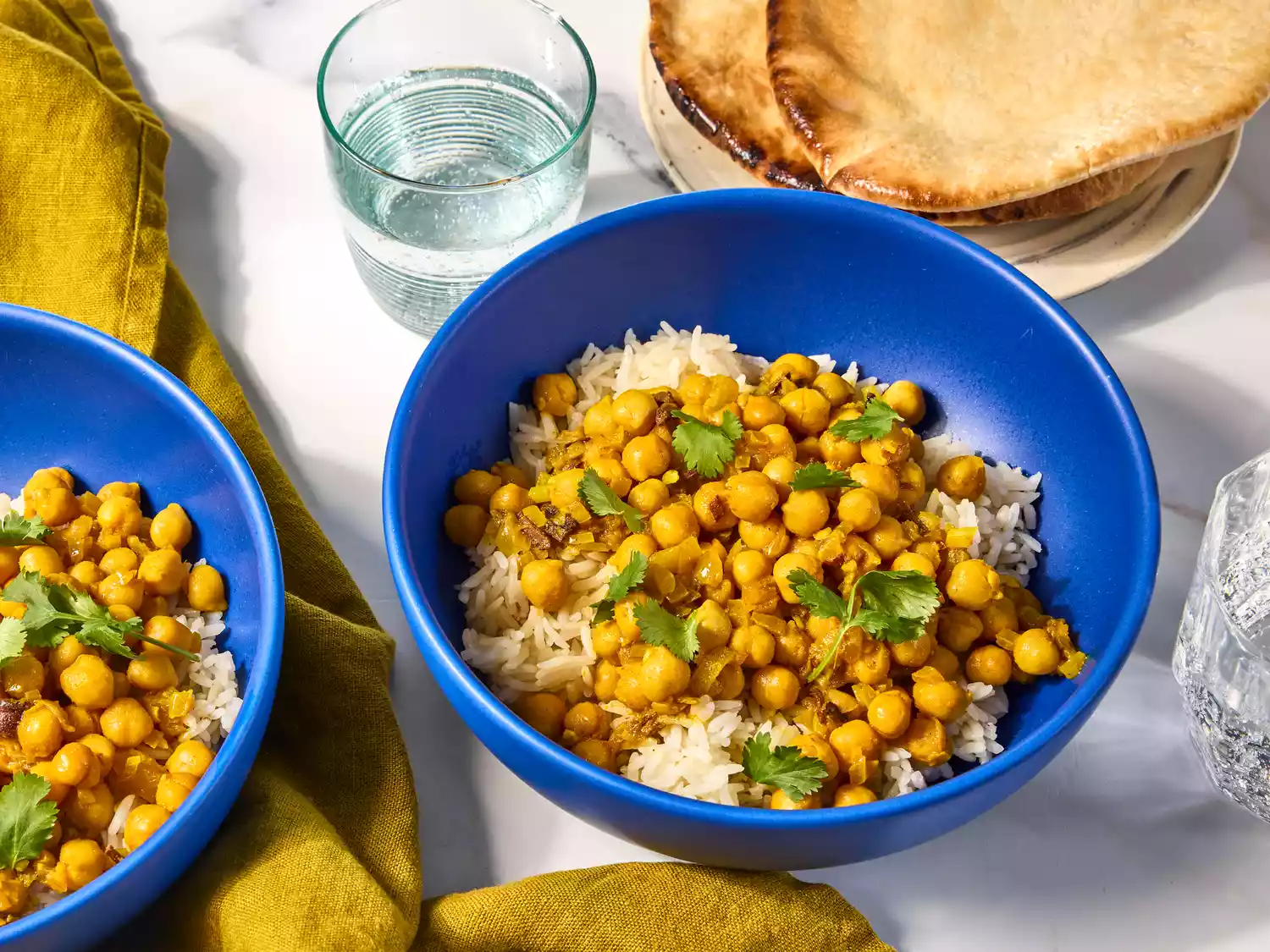 Chickpea curry served over rice in blue bowls with pita.
