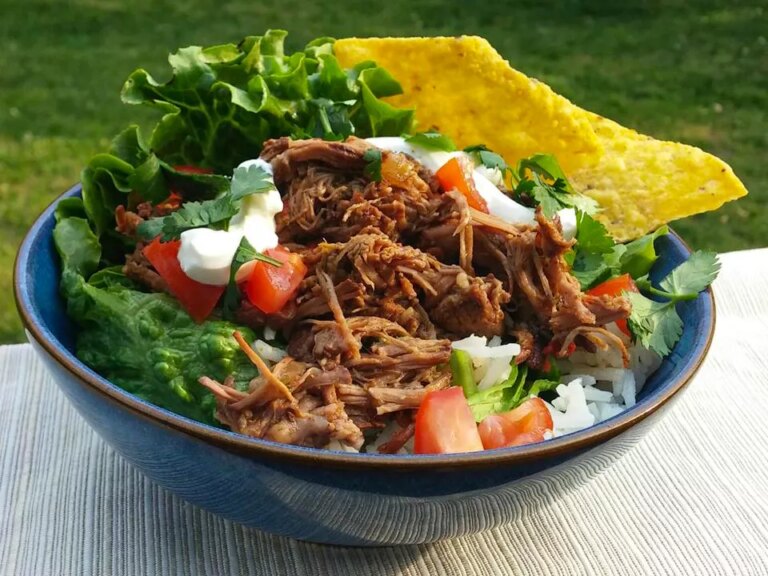 Close up view of chipotle barbacoa in a bowl with rice, tomatoes, fresh herbs, sour cream, lettuce and a tortilla