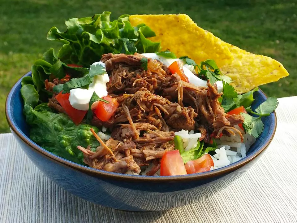 Close up view of chipotle barbacoa in a bowl with rice, tomatoes, fresh herbs, sour cream, lettuce and a tortilla